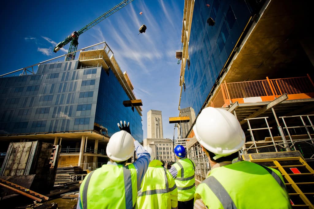 Site team in hard hats and high-visibility vests looking up at a multi-storey building under construction, with a tower crane overhead